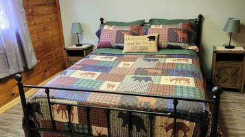 Ein Bett mit einer Quiltdecke mit Tiermotiven, zwei Nachttischlampen, ein gerahmtes Bild an der Wand und Holzpaneele.