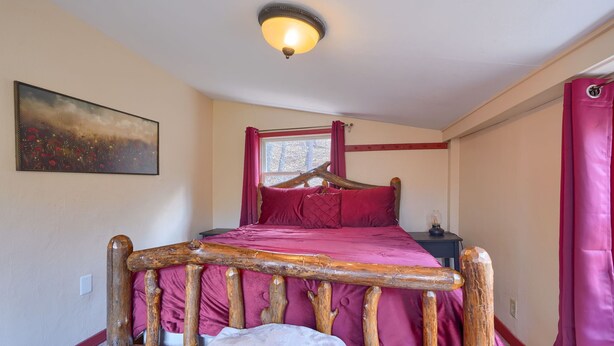 Une chambre à coucher avec un cadre de lit en bois, une couverture rouge, une table de chevet, une lampe et un tableau accroché au mur.