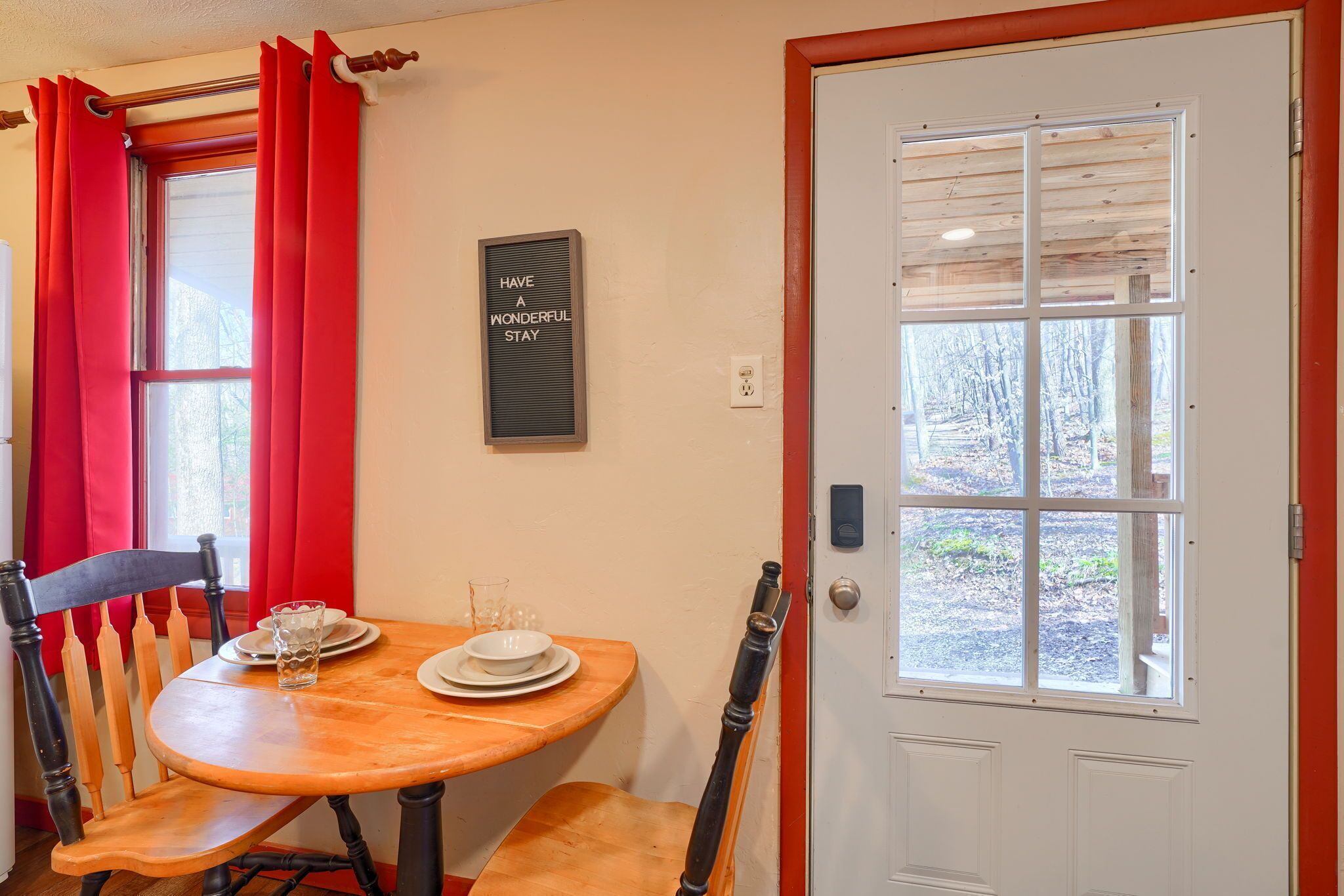 A dining area with a wooden table, two chairs, a glass of water, and a plate. A door with a window is visible in the background.