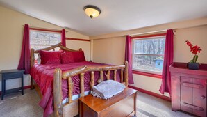 Quarto com cama de madeira, mesa de cabeceira, cômoda e janela com cortinas vermelhas.