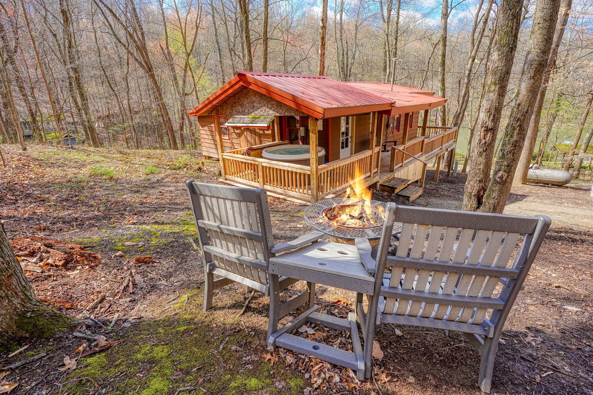 Eine Holzhütte mit Terrasse und Whirlpool, umgeben von Bäumen.
