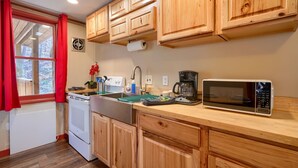 Une cuisine avec des meubles de rangement en bois, une cuisinière, un four à micro-ondes et une fenêtre ornée de rideaux rouges.