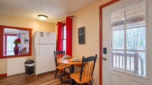 Une cuisine compacte comprenant un réfrigérateur, une table à manger avec des chaises, une fenêtre donnant sur des arbres et une porte avec une pancarte.