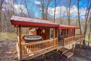A wooden cabin with a hot tub and deck, surrounded by trees.