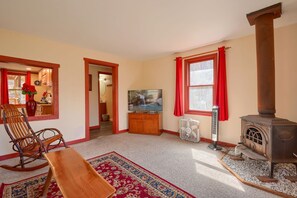 A cozy living room with a rocking chair, a TV, a fireplace, and a kitchen visible through an open door.