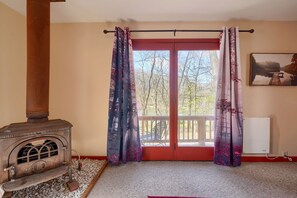 A room with a wood-burning stove, a balcony with a view of trees, and a painting on the wall.