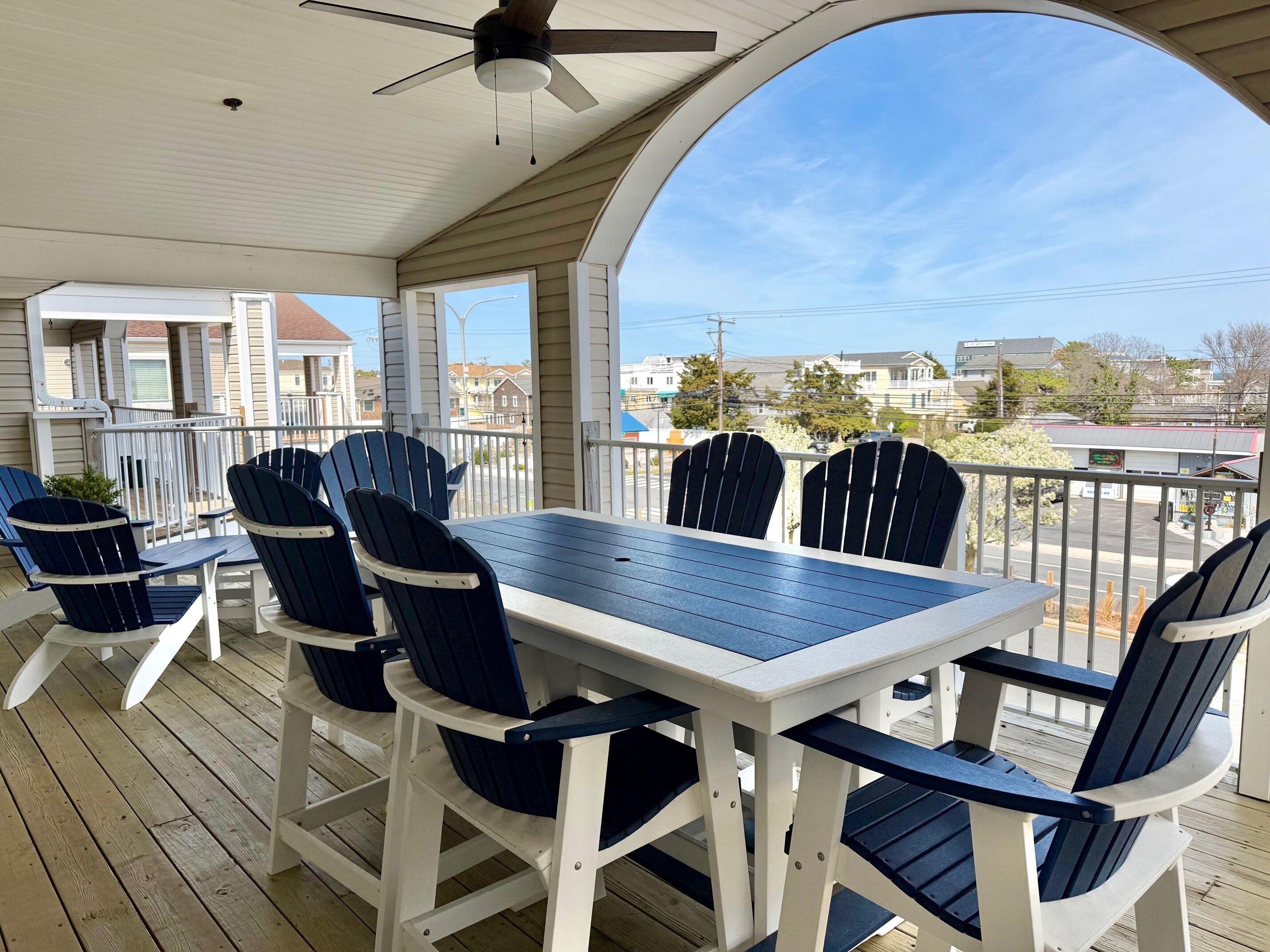 A covered outdoor seating area with a table and chairs, a ceiling fan, and a view of the neighborhood.