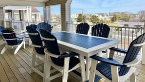 A covered outdoor seating area with a table and chairs, a ceiling fan, and a view of the neighborhood.