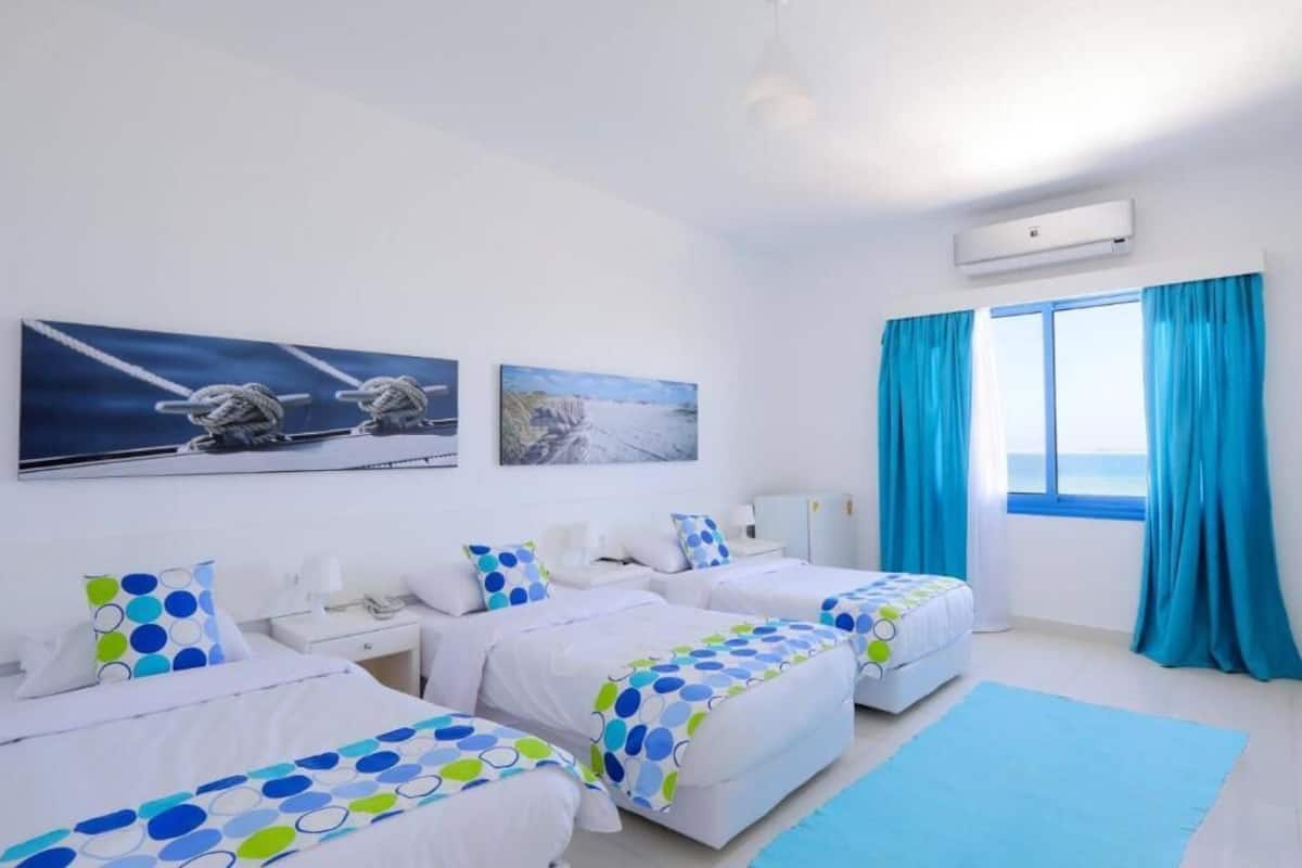 A hotel room with two beds, a desk, a chair, a window with curtains, and artwork on the wall.