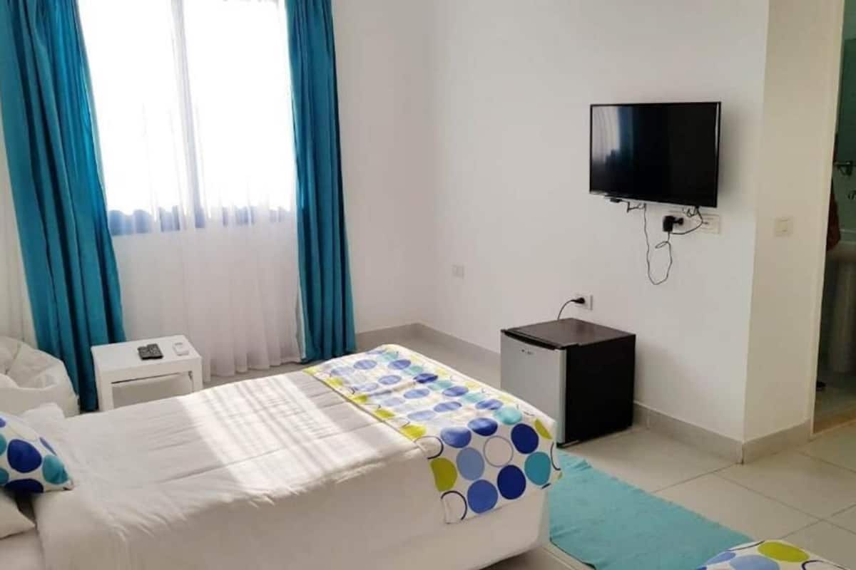 A hotel room with a bed, a desk, a TV, and a bathroom visible through an open door.
