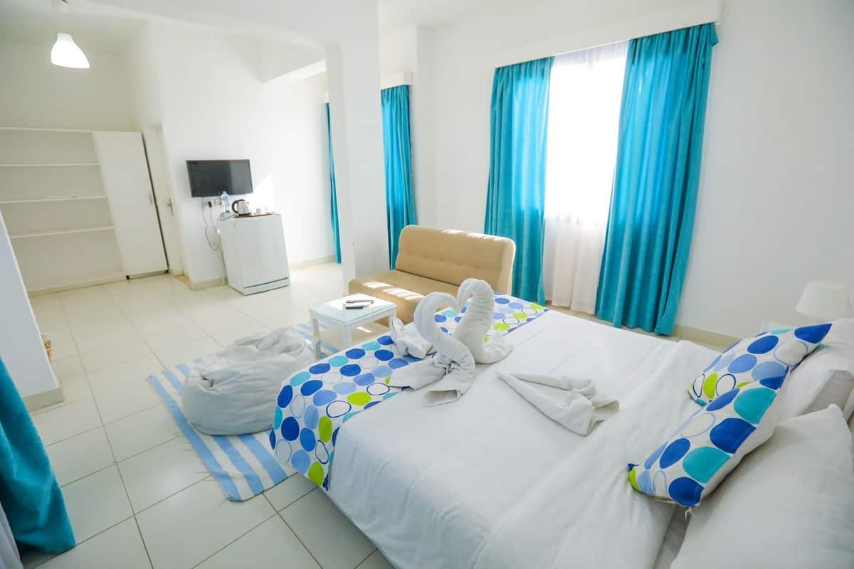 A hotel room with a bed, a sofa, a TV, a small table, and a window with curtains.