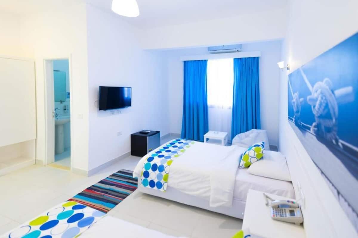 A hotel room with a bed, a TV, a desk, and a bathroom visible through an open door.