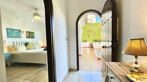 Une chambre d’hôtel avec un lit, une table de chevet, une lampe et une vue sur une cour intérieure donnant sur une porte menant à l’extérieur.