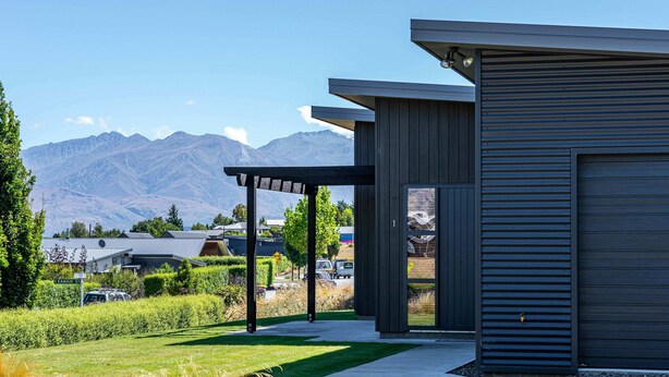 A modern building with a garage door, a covered patio, and a view of mountains in the background. - Hoheria Mountain Lodge (Wānaka)