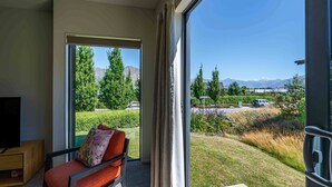A balcony with a sofa and a TV, overlooking a well-maintained garden and distant mountains. - Hoheria Mountain Lodge (Wānaka)