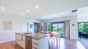 A spacious kitchen with a large island, a dining area with a table and chairs, and a view of the outdoors through large windows. - Hoheria Mountain Lodge (Wānaka)