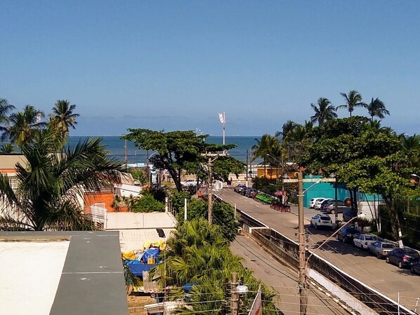 Eine Küstenlandschaft mit einer Straße, gesäumt von parkenden Autos und Palmen, die zum Strand führt.