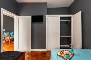 Ein Schlafzimmer mit einem Bett, einem Nachttisch mit einem Frühstücksbrettchen, einem an der Wand montierten Fernseher und einem Kleiderschrank mit Kleidung.