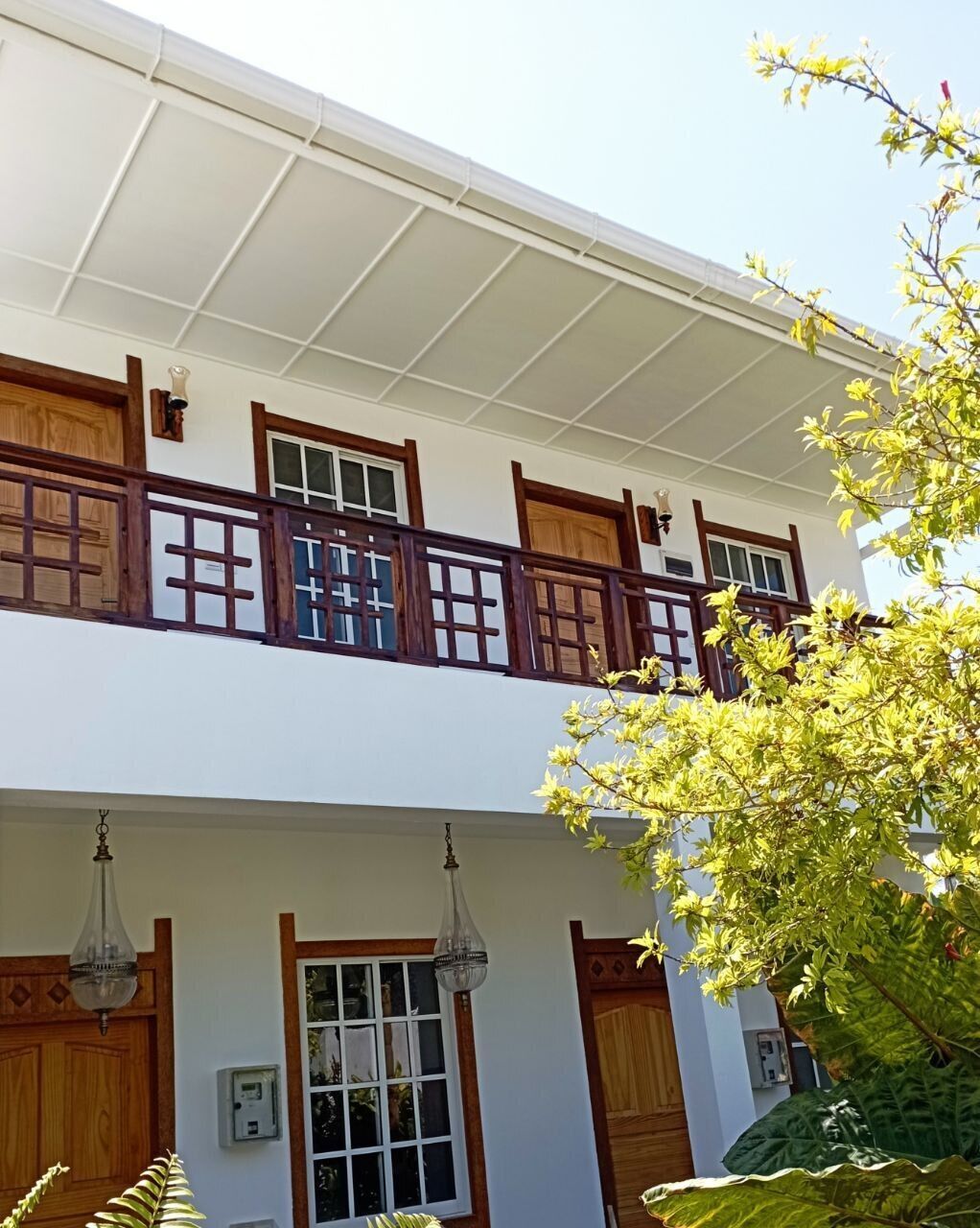 A two-story building with wooden balconies, large windows, and a covered entrance area.