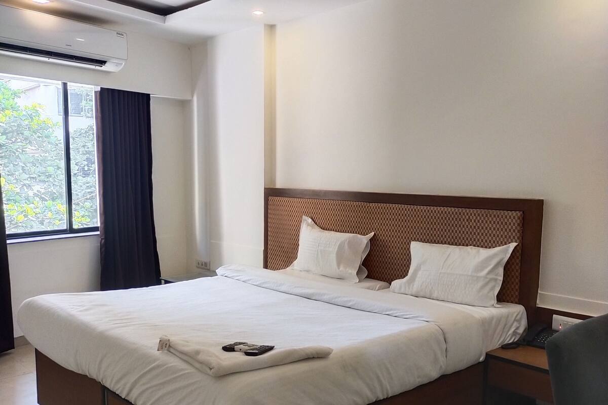 A hotel room with a large bed, a ceiling fan, a window with curtains, and a bedside table with a lamp.