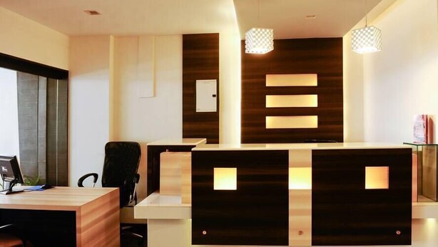 A reception desk with a modern design, featuring a combination of wood and dark panels. There are two pendant lights above the desk, and a small shelf with a vase on the right side. - Hotel Ace Residency (Mumbai)