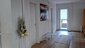 A spacious room with wooden flooring, a white door, a painting on the wall, and a small white bench. - Ferienwohnung Direkt in Wehrheim (Wehrheim)