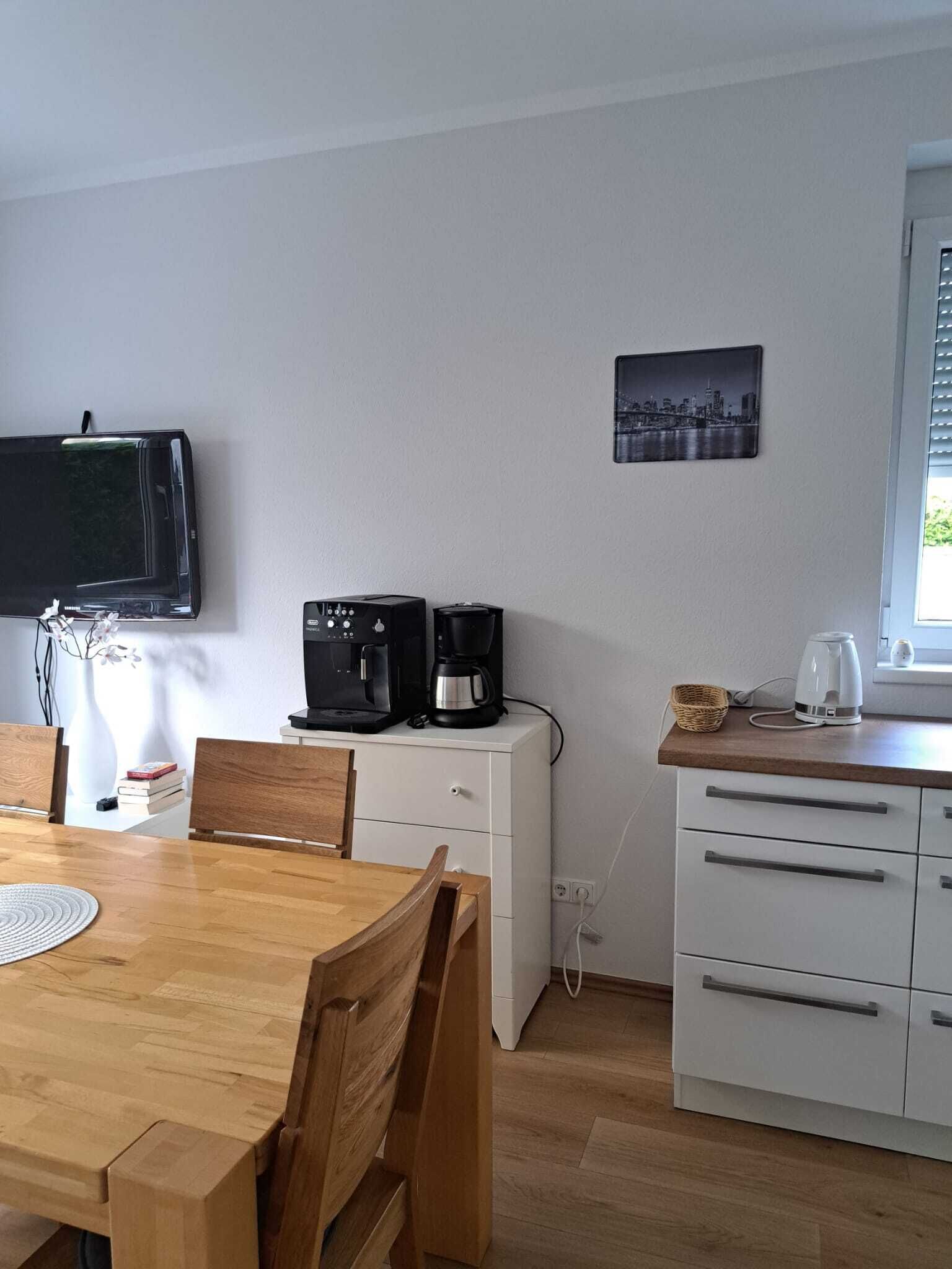 Una pequeña kitchenette con cafetera, hervidor y televisor montado en la pared.