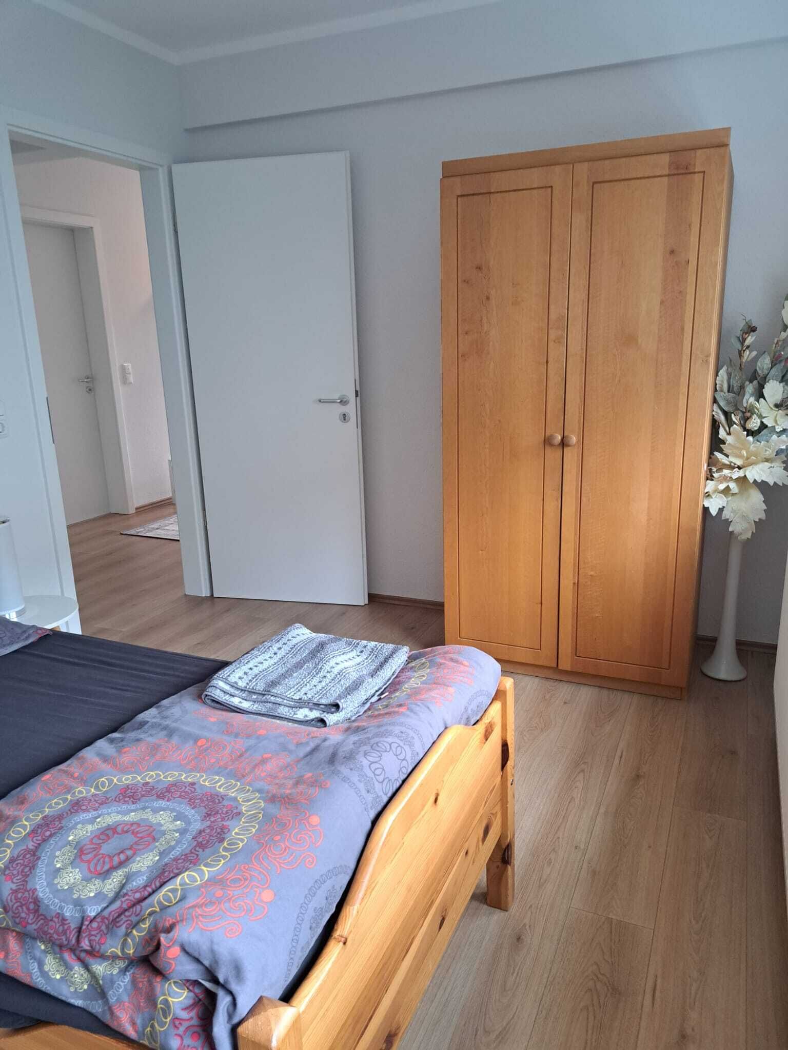 Een slaapkamer met een bed, een houten kledingkast en een deur naar een andere kamer.
