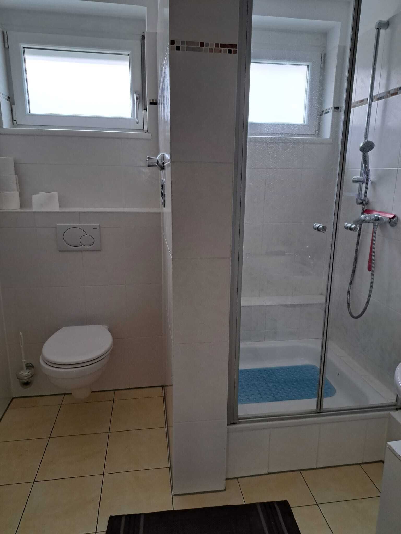 Een compacte badkamer met toilet, douchecabine en een raam boven het toilet.