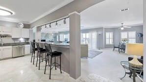 A spacious kitchen with a central island, bar stools, and a dining area with a table and chairs. - Harbor Central Penthouse (Destin)