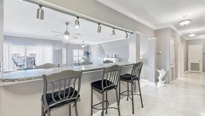 A modern kitchen with a large island, bar stools, pendant lighting, and a view of the city. - Harbor Central Penthouse (Destin)