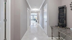 A hallway with white walls, a tiled floor, and a stone fireplace. - Harbor Central Penthouse (Destin)