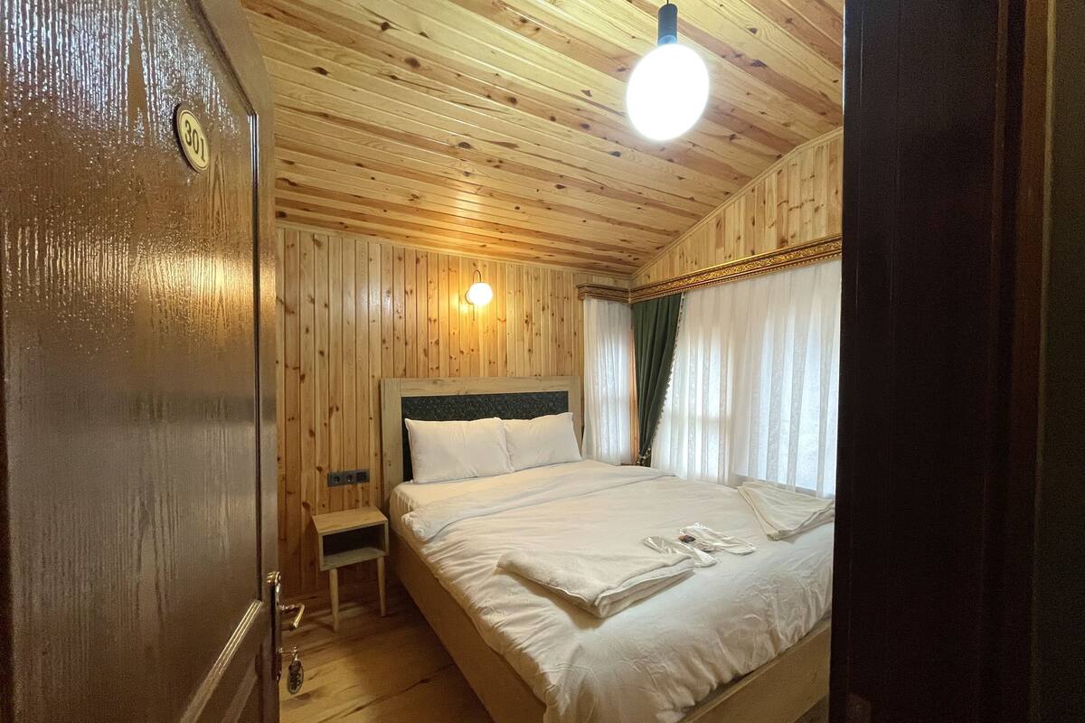 Ein Zimmer mit Holzwänden, einem Bett, einem Nachttisch und einer Wandleuchte.