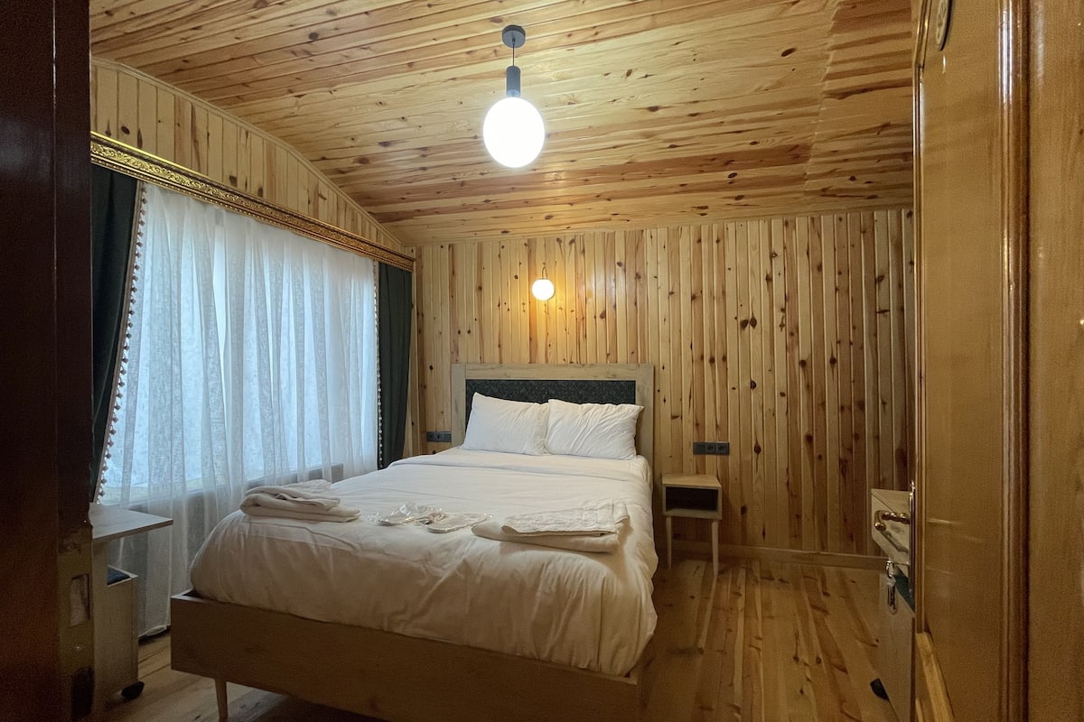 Ein Zimmer mit Holzwänden, einem Bett, einem Nachttisch und einer Wandleuchte.