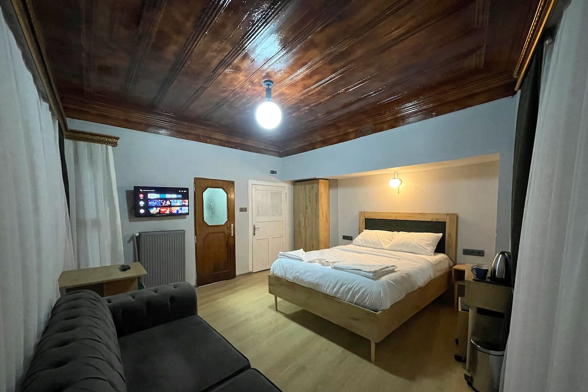 Ein Schlafzimmer mit Holzboden, einem Bett mit weißer Bettwäsche, einem hölzernen Kopfteil, einem kleinen Nachttisch, einem Heizkörper, einem Fernseher und einer Tür mit Milchglasfenster.