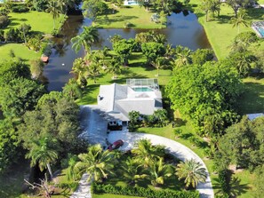 Vista aèria d'una casa amb piscina, envoltada de vegetació exuberanta i una petita bassa.