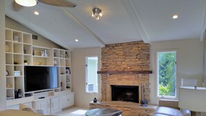 Una sala de estar moderna con chimenea de piedra, un televisor de pantalla plana grande, estanterías empotradas y una zona de estar cómoda.