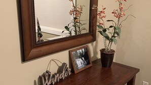 Une console en bois, avec un miroir au-dessus, une photo encadrée et une plante en pot aux fleurs rouges.