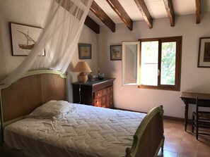 Ein Schlafzimmer mit Bett, Nachttisch, Lampe, Kommode und Fenster.