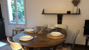 Une table de salle à manger ronde, entourée de quatre chaises, une petite étagère au-dessus, sur laquelle sont disposés des objets décoratifs, et une fenêtre donnant sur un paysage verdoyant.