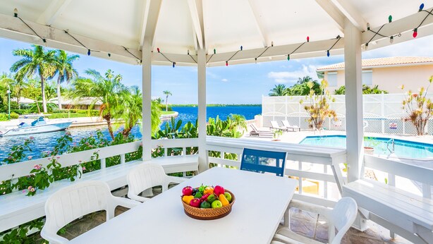 A covered outdoor seating area with a table and chairs, a fruit bowl, a pool, and a view of the ocean. - Private Luxury Waterfront Villa with Pool (West Bay)
