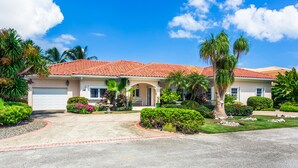 A two-story house with a red-tiled roof, a front porch, and a well-maintained garden with various plants and a palm tree. - Private Luxury Waterfront Villa with Pool (West Bay)