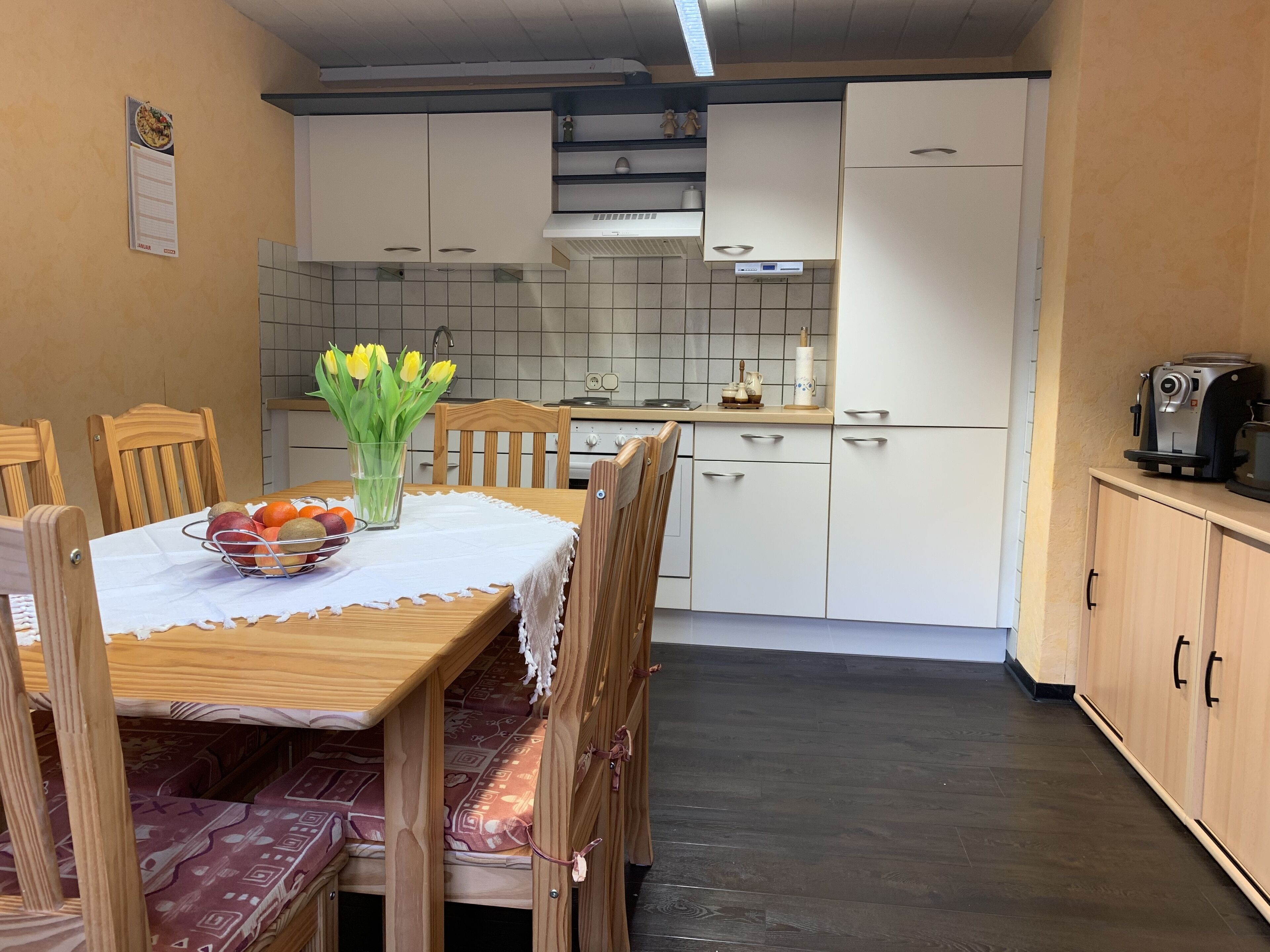 A compact kitchen with white cabinets, a dining table with chairs, and a coffee machine.