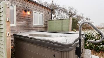 Een hottub voor een houten huis met een raam en een groene hek achtergrond.