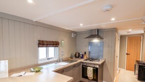 A modern kitchen with a central island, stainless steel appliances, and a window with a plaid valance. - Grouse Lodge (Scarborough)