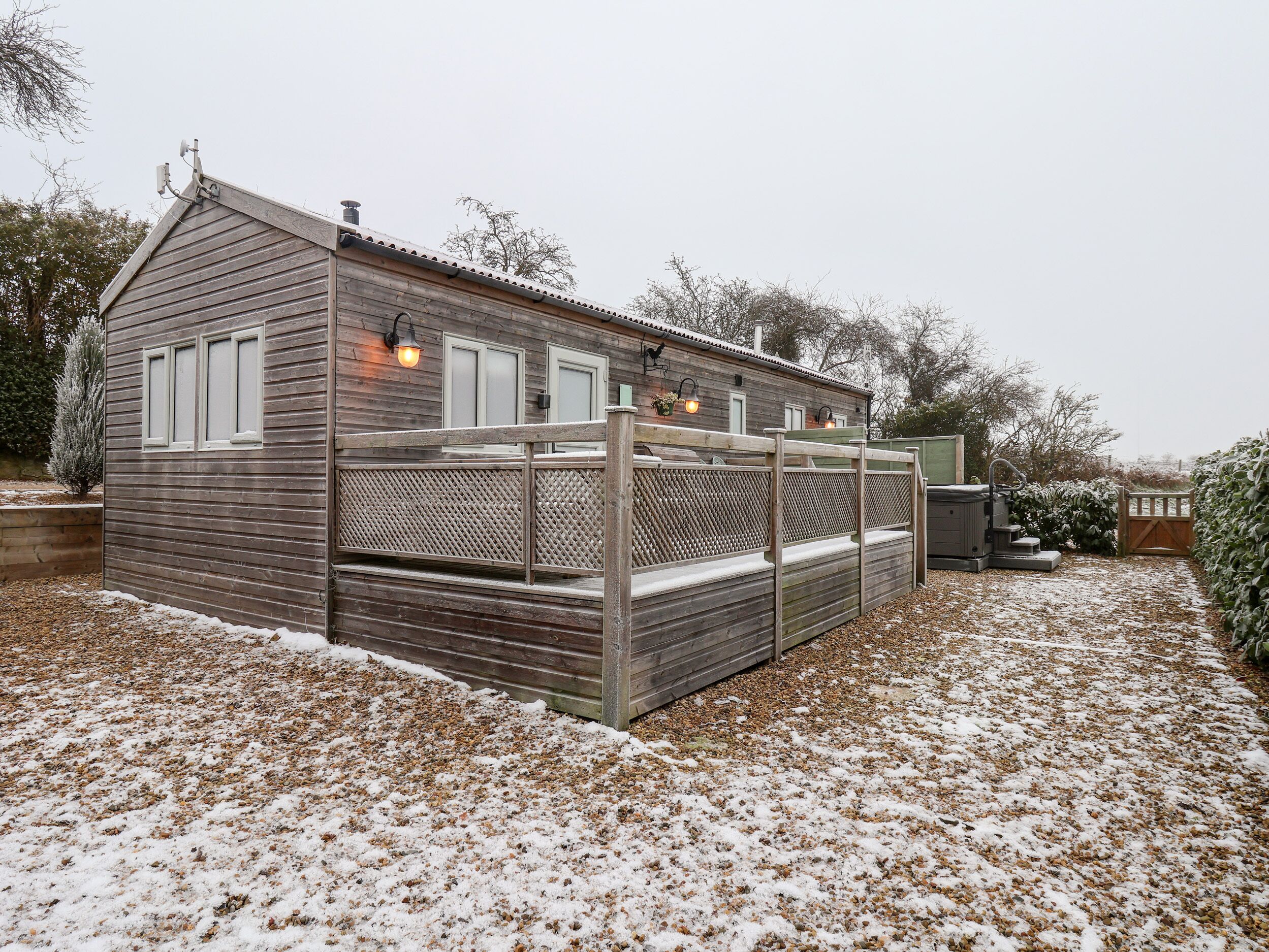 Een houten blokhut met een overdekt terras, een schoorsteen en een klein bijgebouwt tuinhuisje.