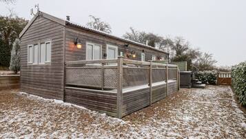 Een houten blokhut met een overdekt terras, een schoorsteen en een klein bijgebouwt tuinhuisje.