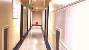 Un pasillo largo y estrecho con puertas a ambos lados, un bote de basura rojo en el centro y una señal de salida verde en el techo.