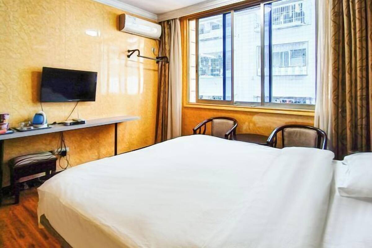 A hotel room with a bed, a desk with a flat-screen TV, a chair, and a window with curtains.