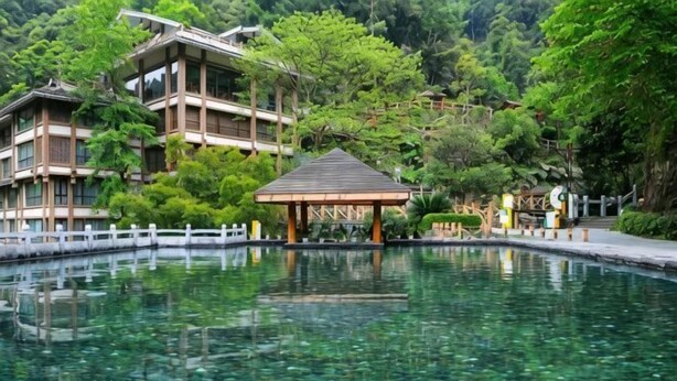 Un edificio japonés tradicional reflejado en un cuerpo de agua cristalina, rodeado de abundante vegetación.
